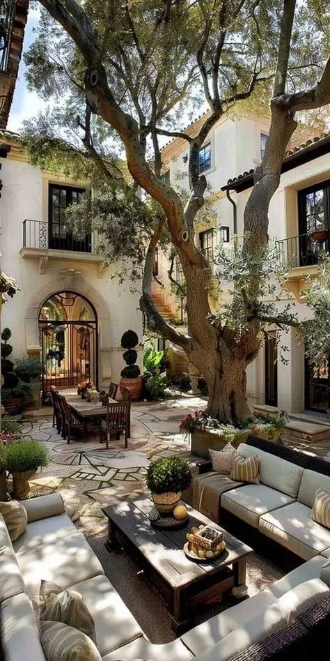 A Mediterranean-style patio featuring an ancient olive tree, cozy seating, and surrounding balconies, embodying the beauty of balconies and patios in Spain.