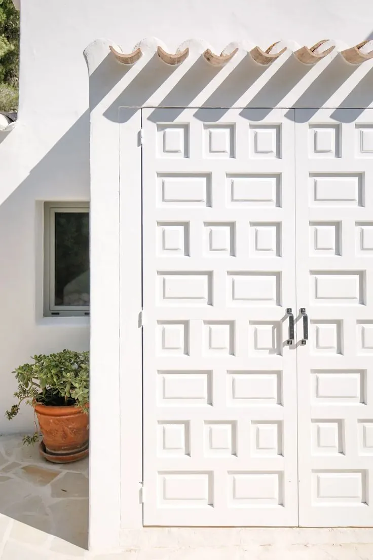 Bright white door with geometric relief pattern on a traditional Mediterranean-style house, next to a potted plant.