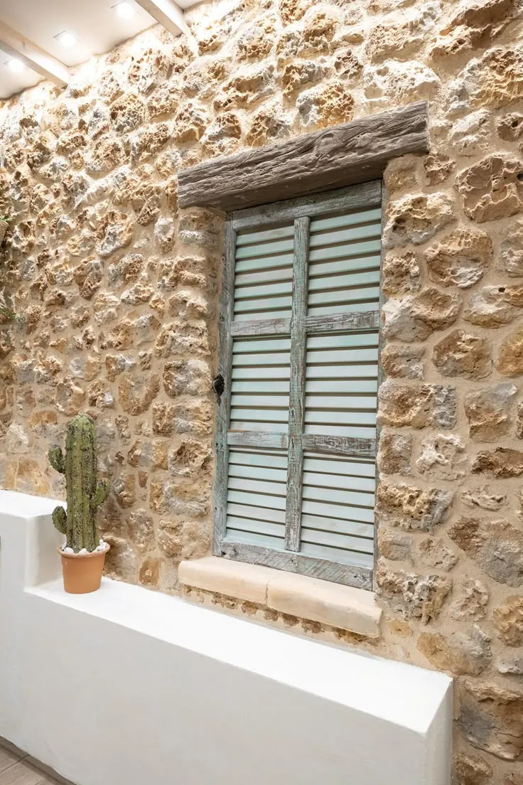 Traditional wooden shutters with a weathered finish on a rustic stone wall, showing materials used in Mediterranean vernacular housing.