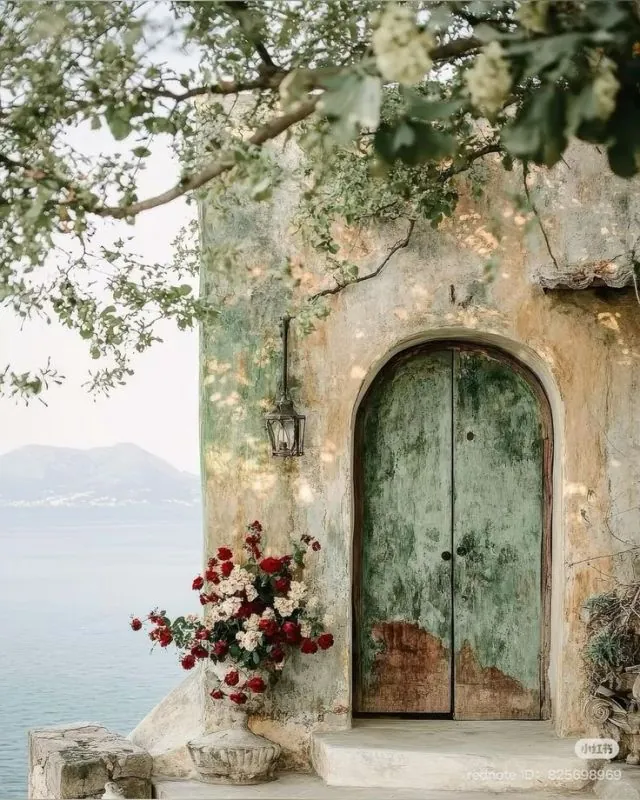 Weathered green arched wooden door on a rustic seaside façade, with floral decoration, reflecting Mediterranean vernacular housing by the coast.