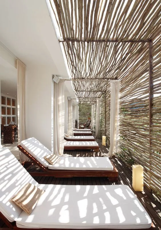 Sunbeds under a slatted stick pergola casting linear shadows with light curtains; shared housing in Alicante and Murcia.